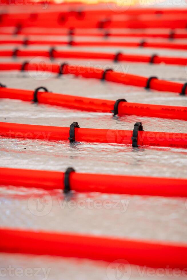 Bright red underfloor heating pipes arranged in parallel lines, secured with black clips on a metallic reflective surface during a heating system installation. photo