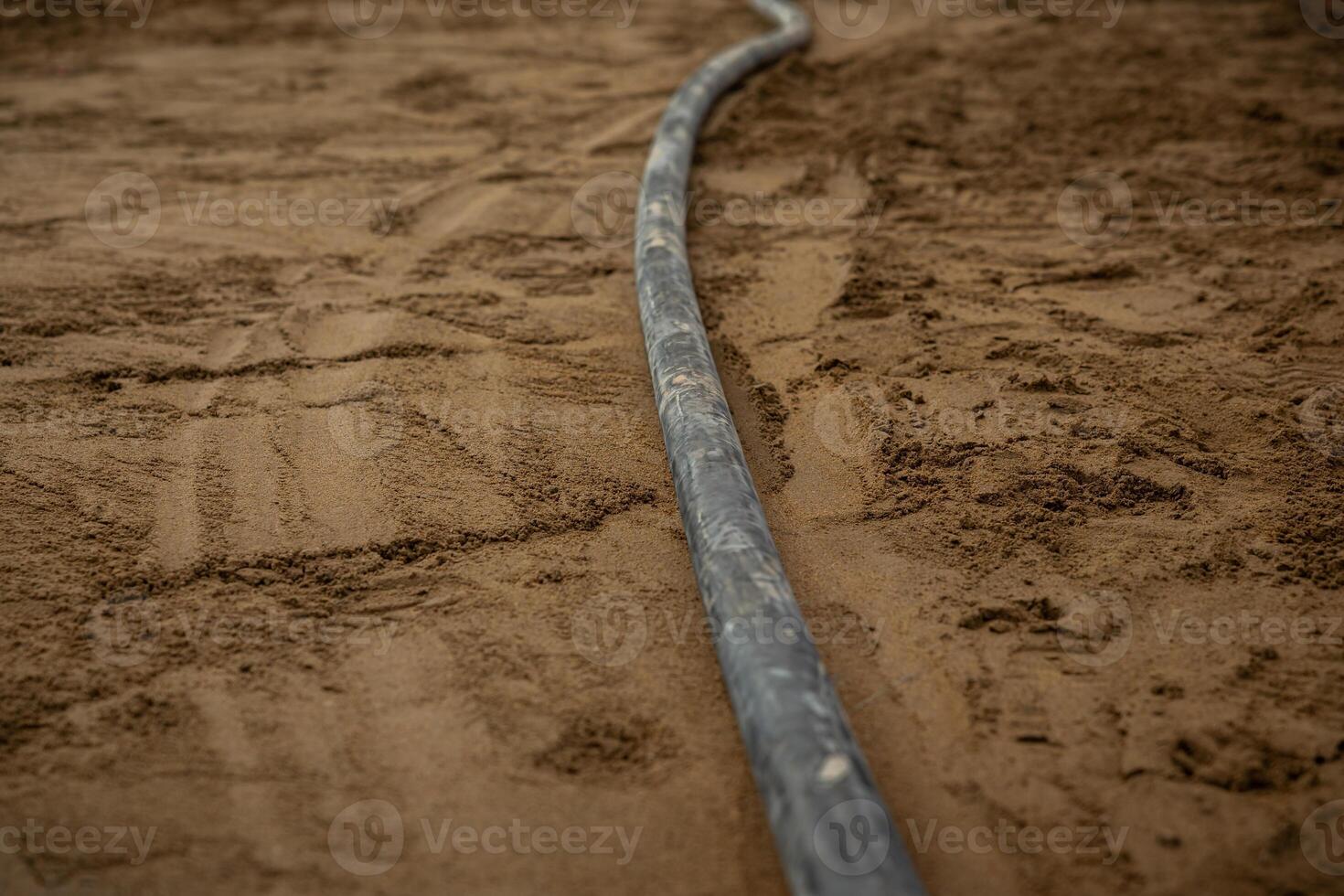 A single underfloor heating pipe curves on compacted sand or soil, with visible ground textures and marks, highlighting early construction stages. photo