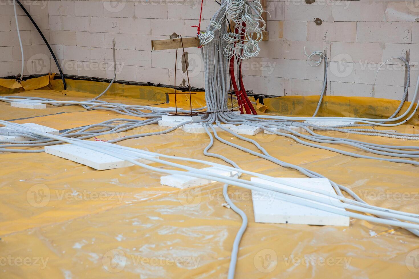 An indoor construction site featuring organized electrical wiring on a yellow floor covering, unfinished white brick walls, and foam blocks on the floor. photo
