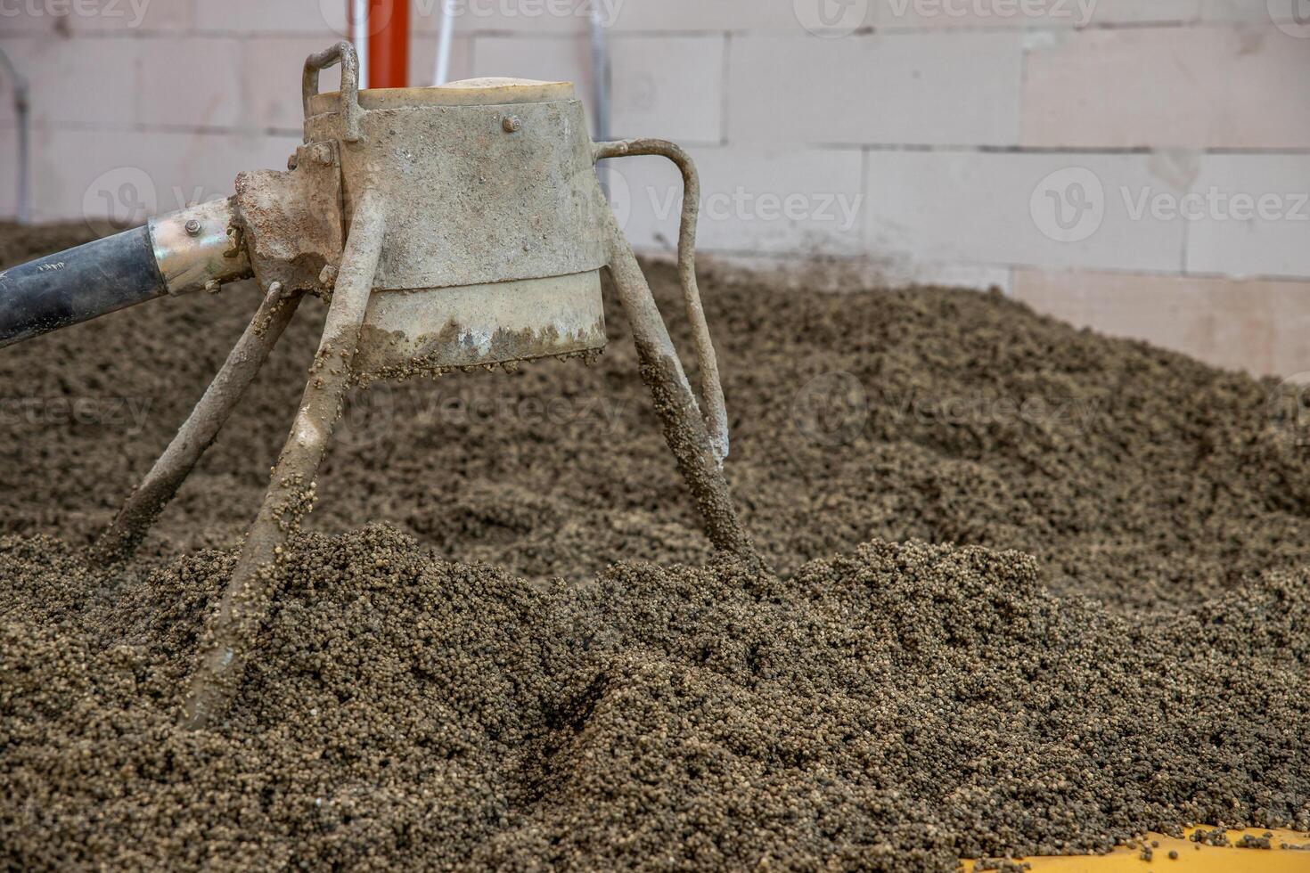 A weathered concrete mixer tool rests in a pile of aggregate material near a partially built brick wall with visible pipes and construction elements. photo