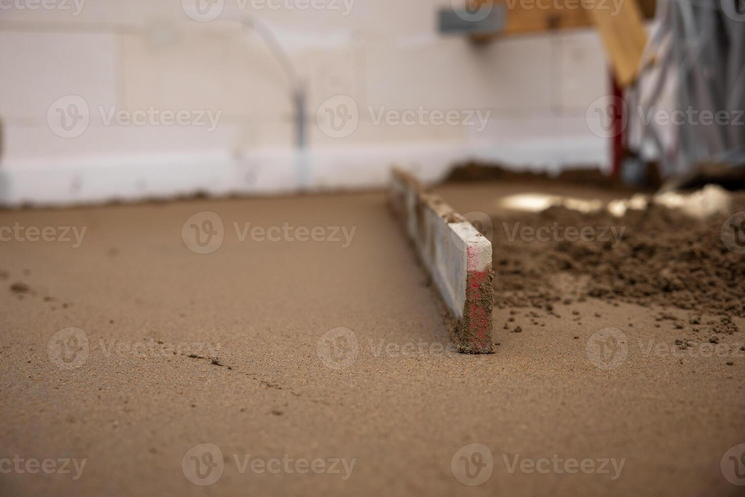 A screed tool levels freshly laid Estrich concrete indoors, with white walls, electrical outlets, and cables visible in the background. photo