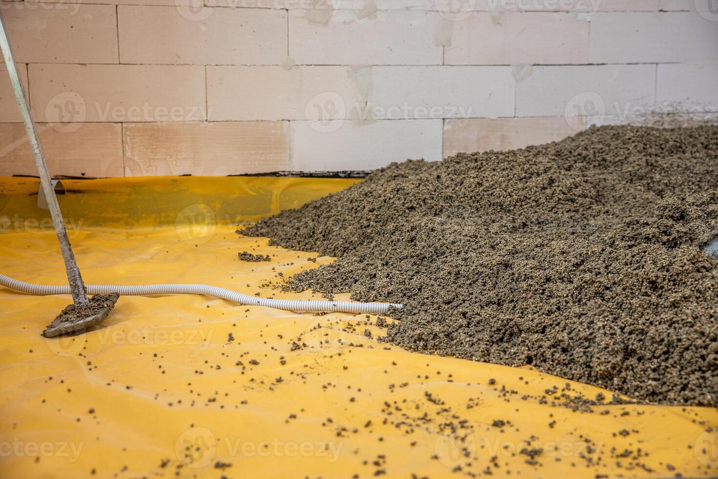 Partially finished interior with a white brick wall, yellow protective sheet on the floor, loose aggregate material, and tools for flooring work. photo