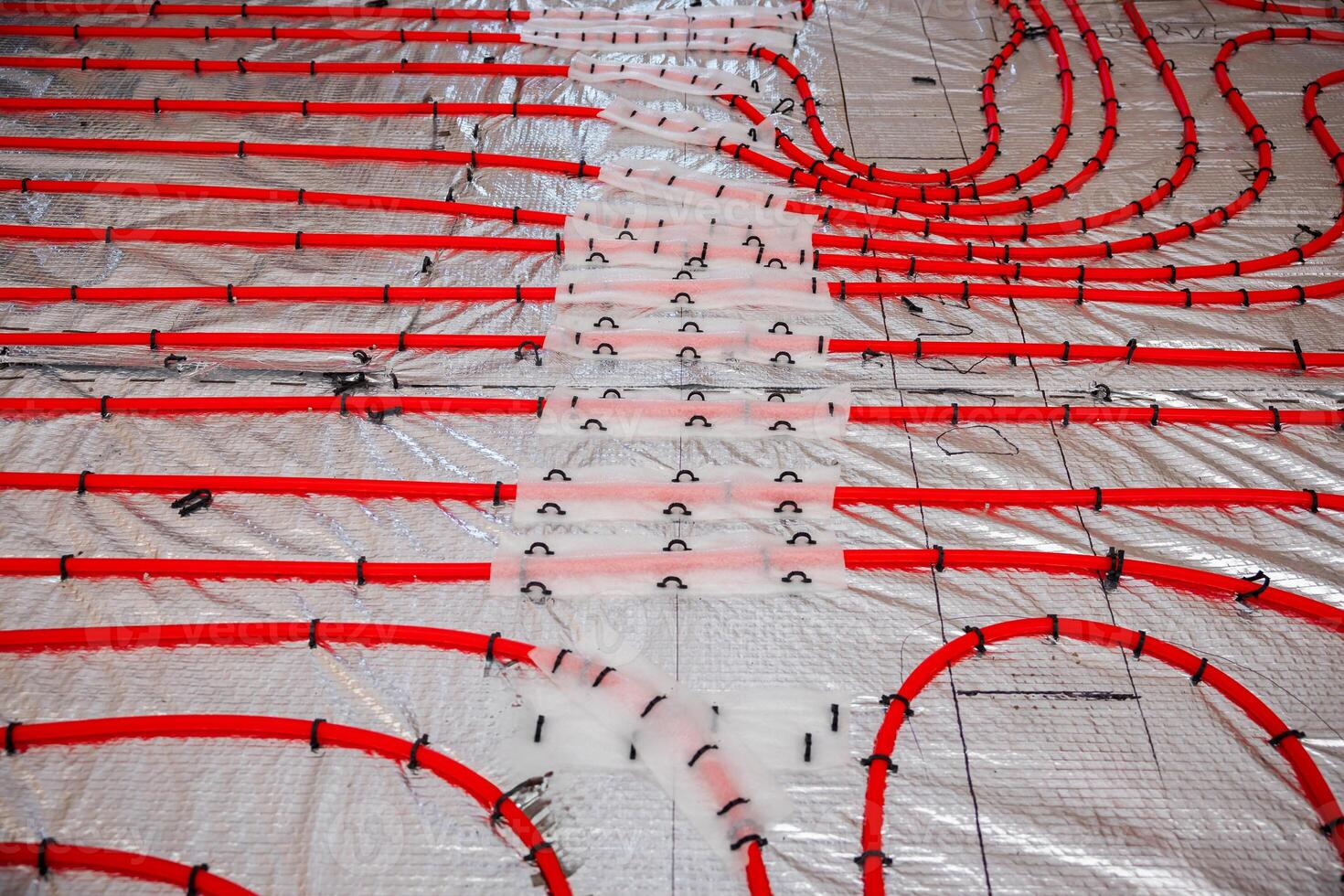 Bright red underfloor heating pipes in a grid pattern secured with clips over a reflective insulation layer, ready for Estrich concrete application. photo