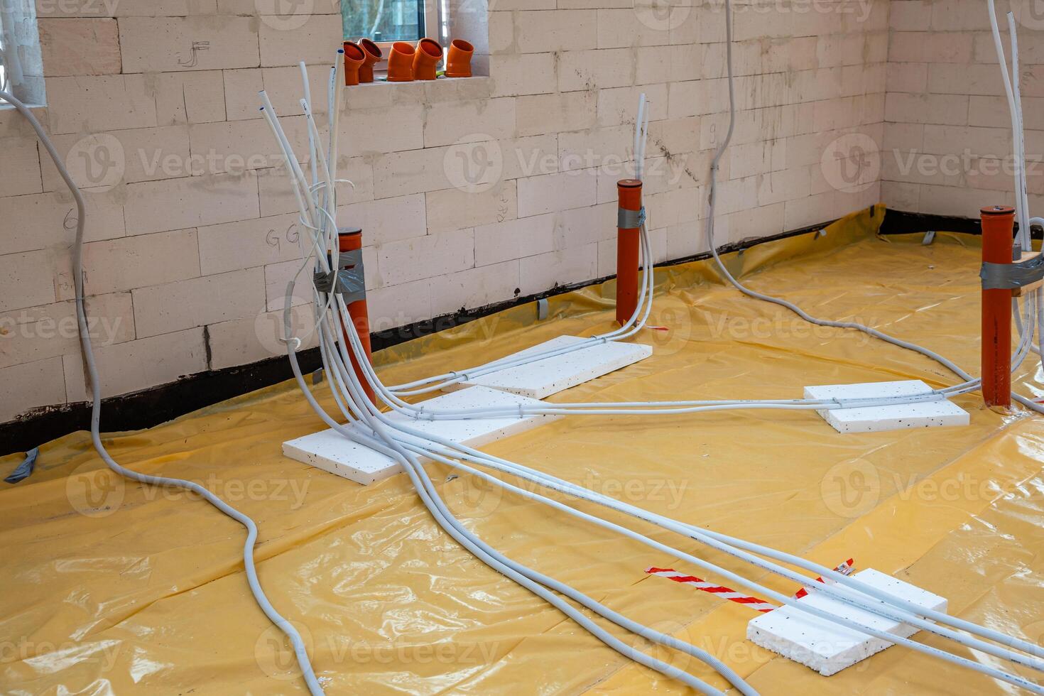 Partially constructed indoor site with white brick walls, yellow floor covering, orange conduit pipes, and white cables secured with foam blocks. photo