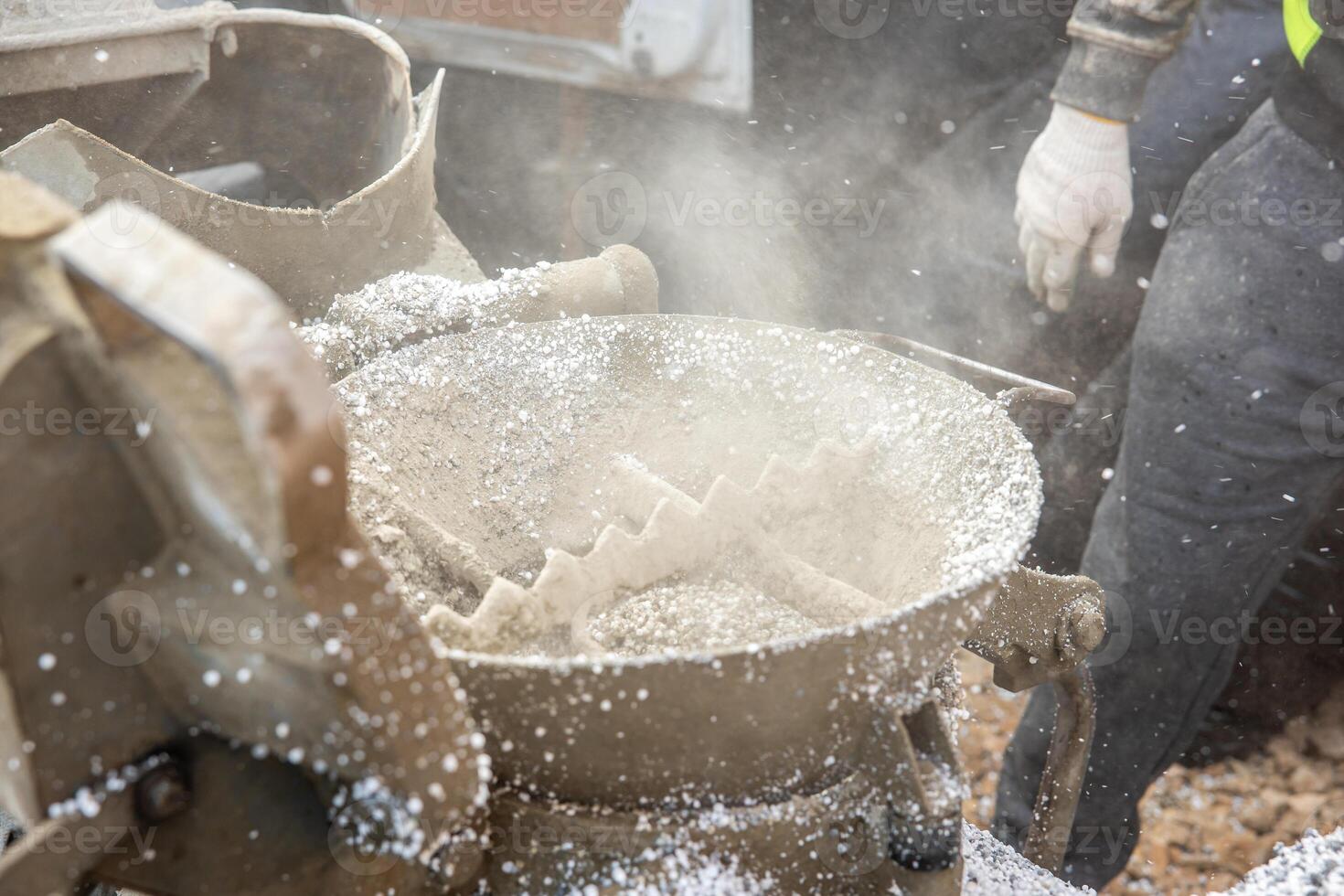 Close up of an industrial machine with a circular toothed mechanism emitting dust, scattered debris, and a worker in gloves and high visibility vest. photo