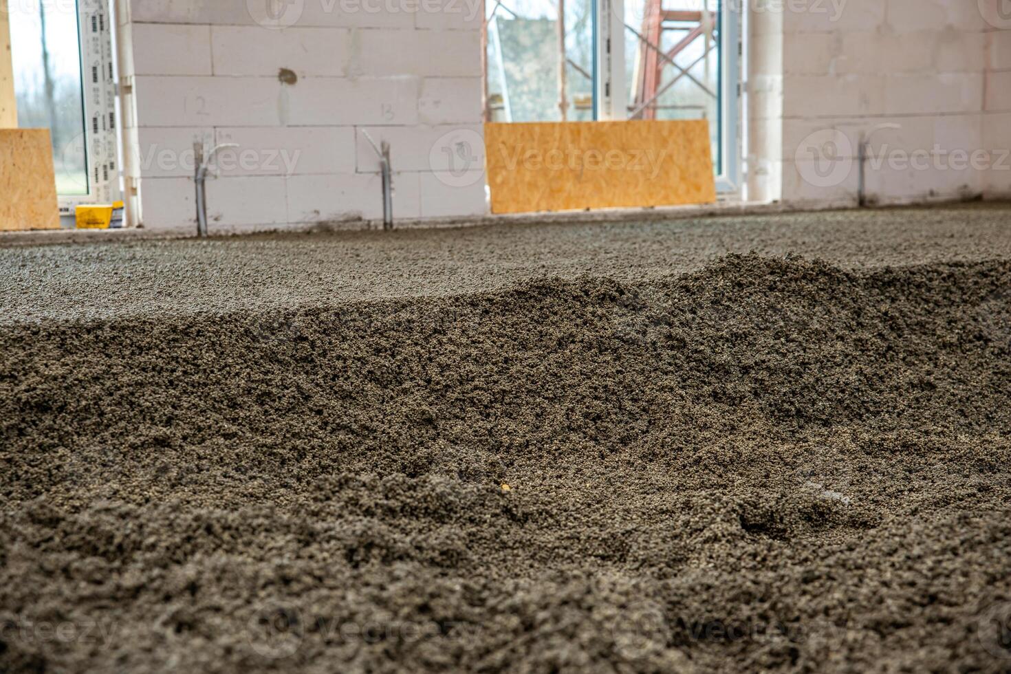 A construction site featuring freshly laid concrete, white block walls with open spaces for windows and doors, and visible scaffolding and materials. photo