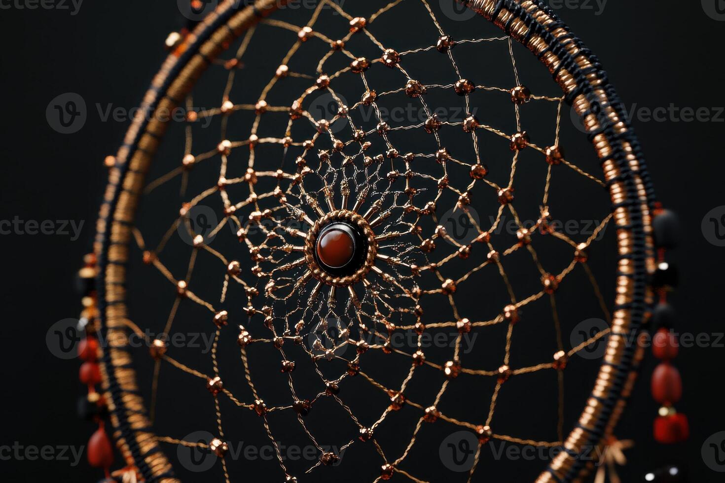 A gold and black dreamcatcher with a red stone in the center photo