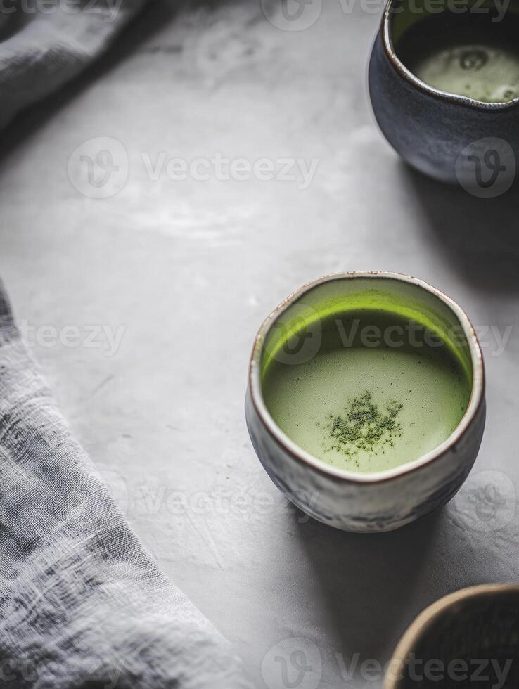 Cup of green tea sits on a table next to two other cups photo