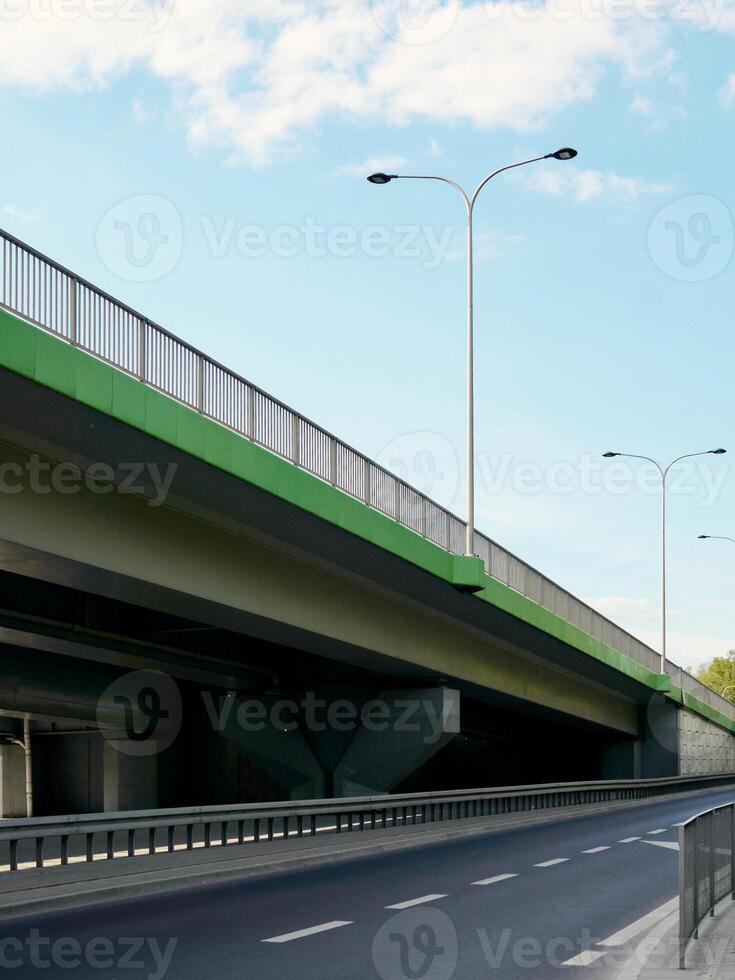 Bridge with a green railing and a street with a white line photo