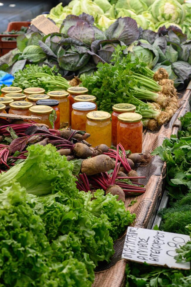 Jars of homemade preserves neatly arranged at an outdoor market, filled with colorful jams, pickles, and sauces photo