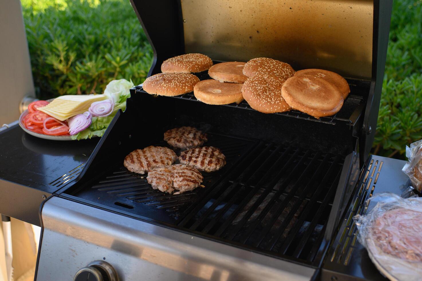 Open-air grilling of burger essentials patties and buns cooking over flame, fresh toppings neatly arranged on a plate beside the grill. photo