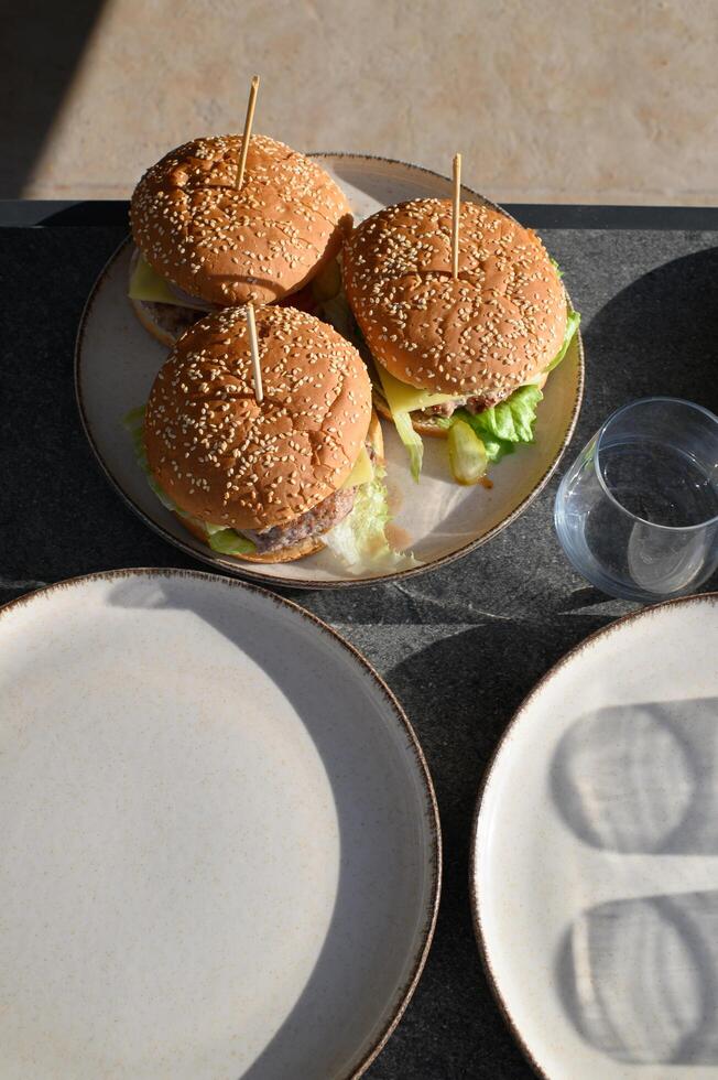 Three delicious burgers stacked with fresh toppings are beautifully served on a table, ready for a summer feast. photo