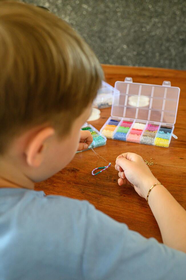 Child focused on making a friendship bracelet, threading tiny beads with concentration, surrounded by organized boxes of colorful beads. photo
