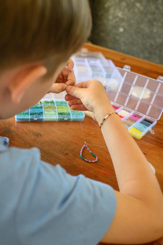 Focused on his project, a boy strings together colorful beads to create a bracelet, using materials spread out before him. photo