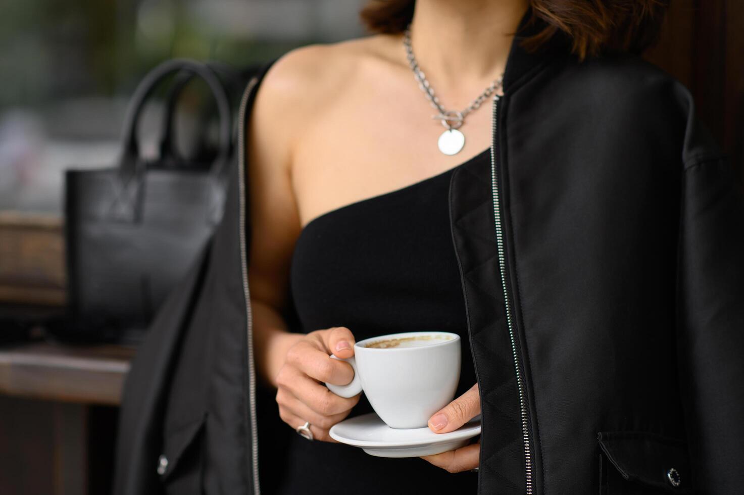 Close-up of a woman s hands near a bar table, gently holding a coffee cup. She is dressed in an all black outfit, giving off a modern and elegant vibe. photo