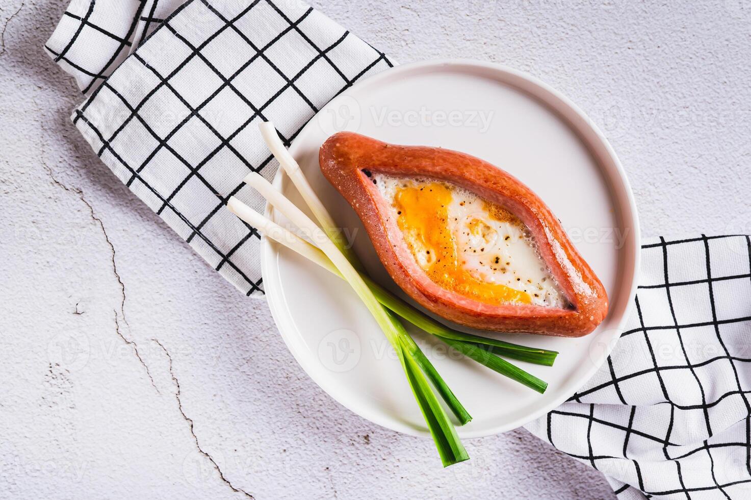 Close up of fried egg in a sausage in the form of khachapuri on a plate on the table top view photo