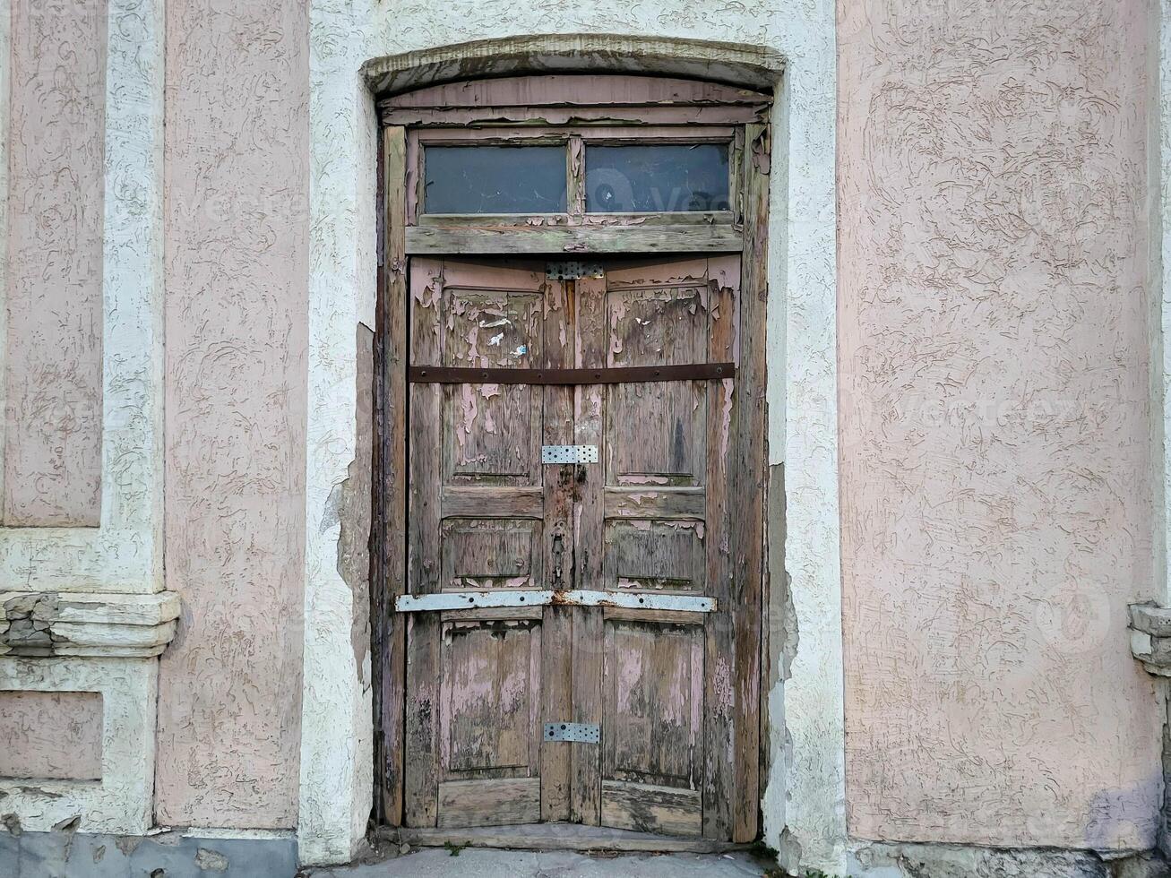 An old wooden battered door on the background of a pink facade. photo