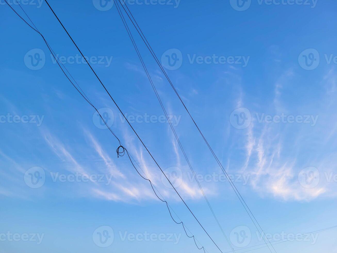 Wires on the background of a light white cloud in the blue sky on a clear, warm day photo