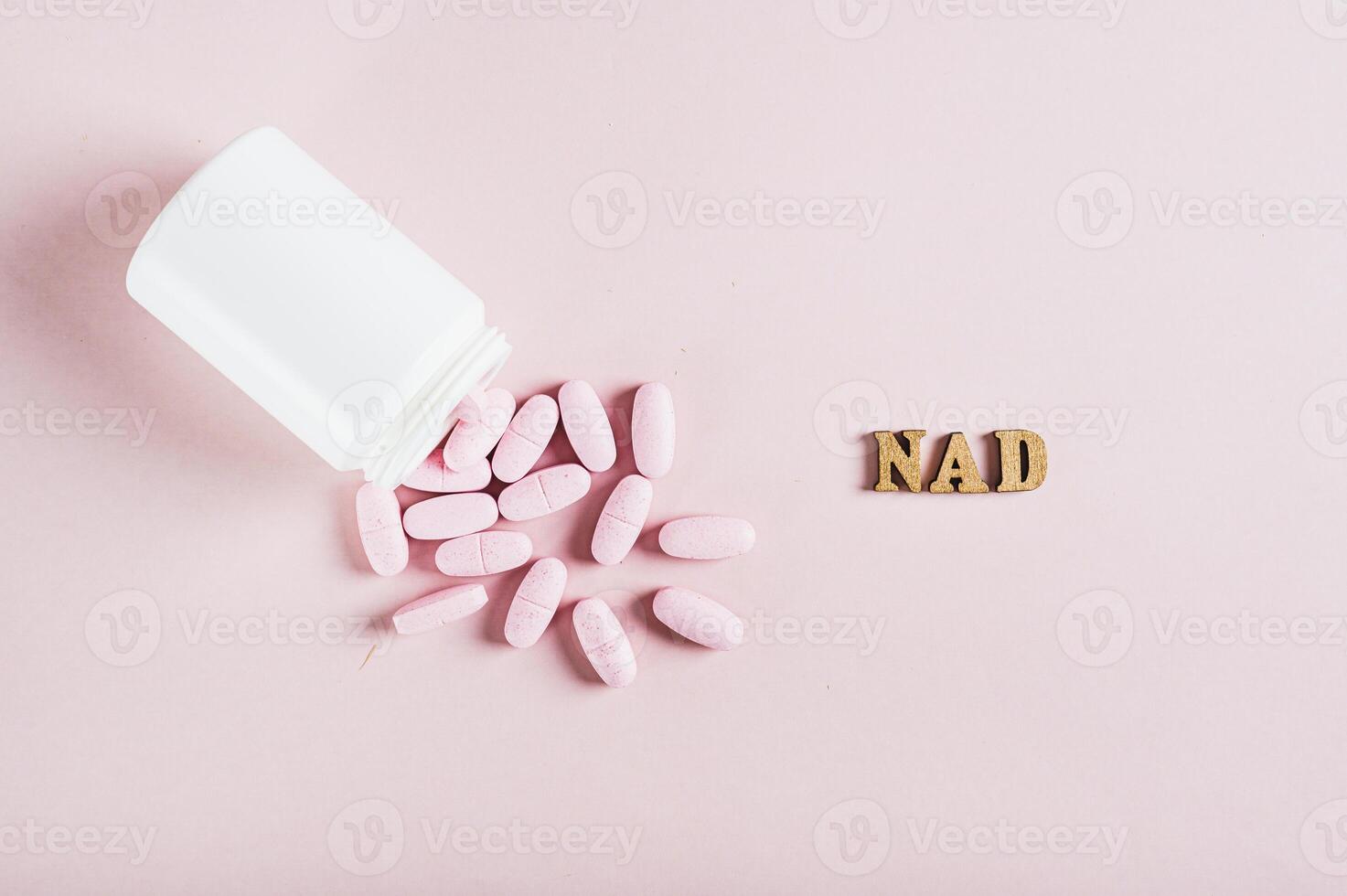 Close up of nicotinamide adenine dinucleotide anti-aging pills and a bottle on pink top view photo