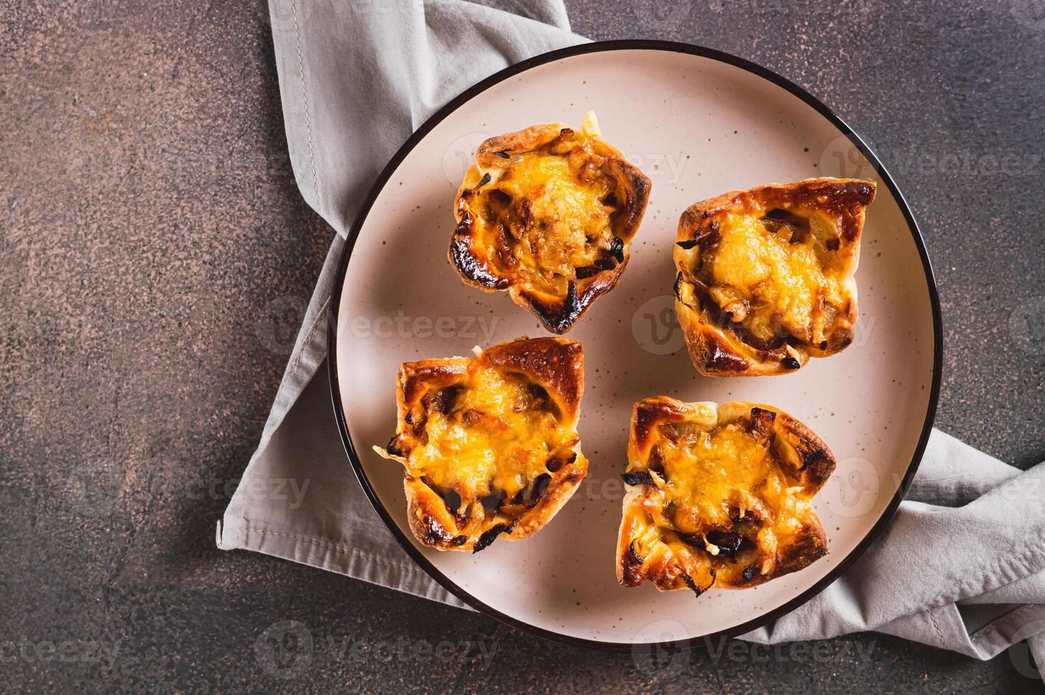 Close up of mini tartlets with caramelized onions and cheese on a plate on a table top view photo