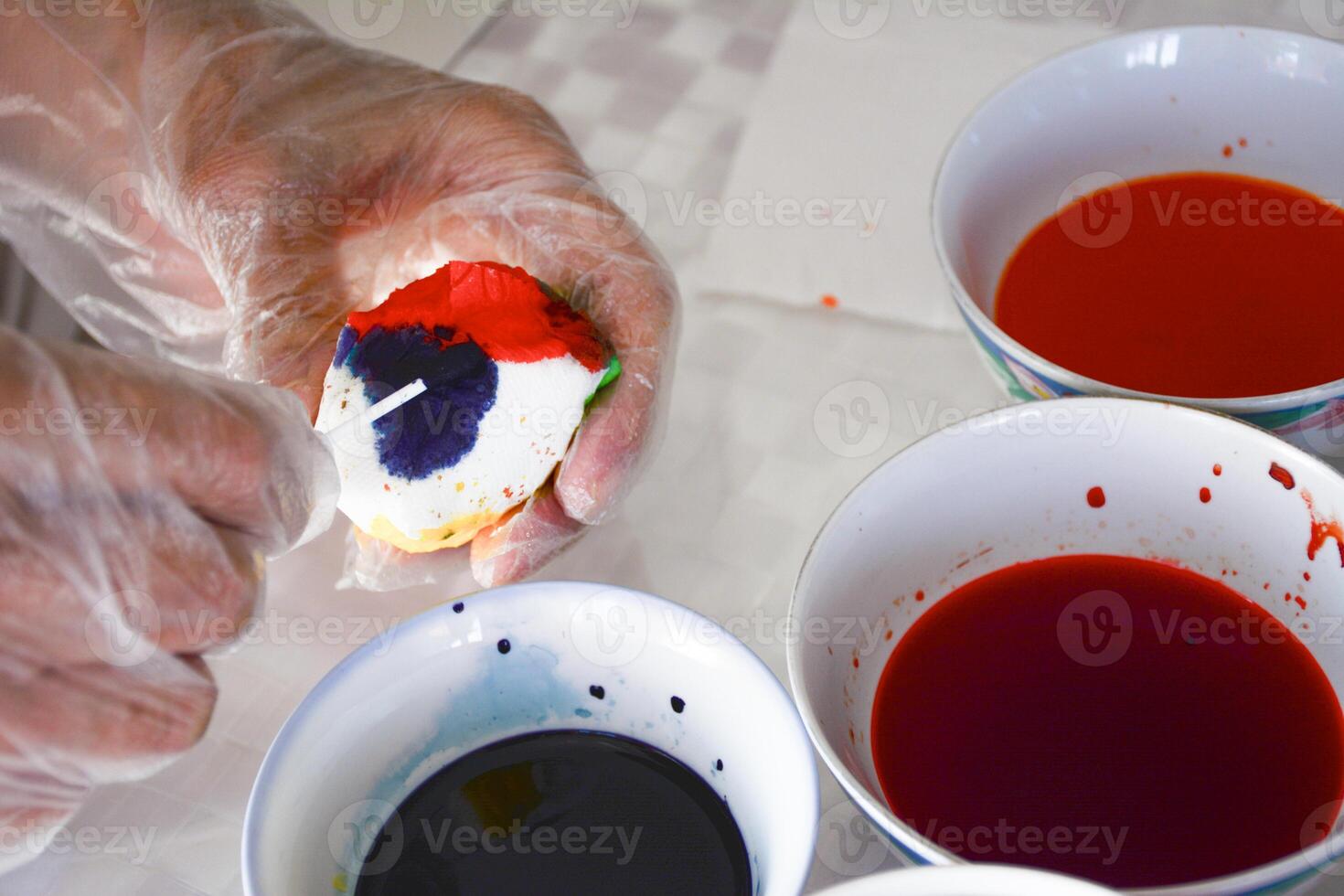activity of coloring Easter eggs. A hand in a protective glove holding an egg and colors it in bright colors. Creativity and festive celebration, traditions associated with Easter egg decorating photo