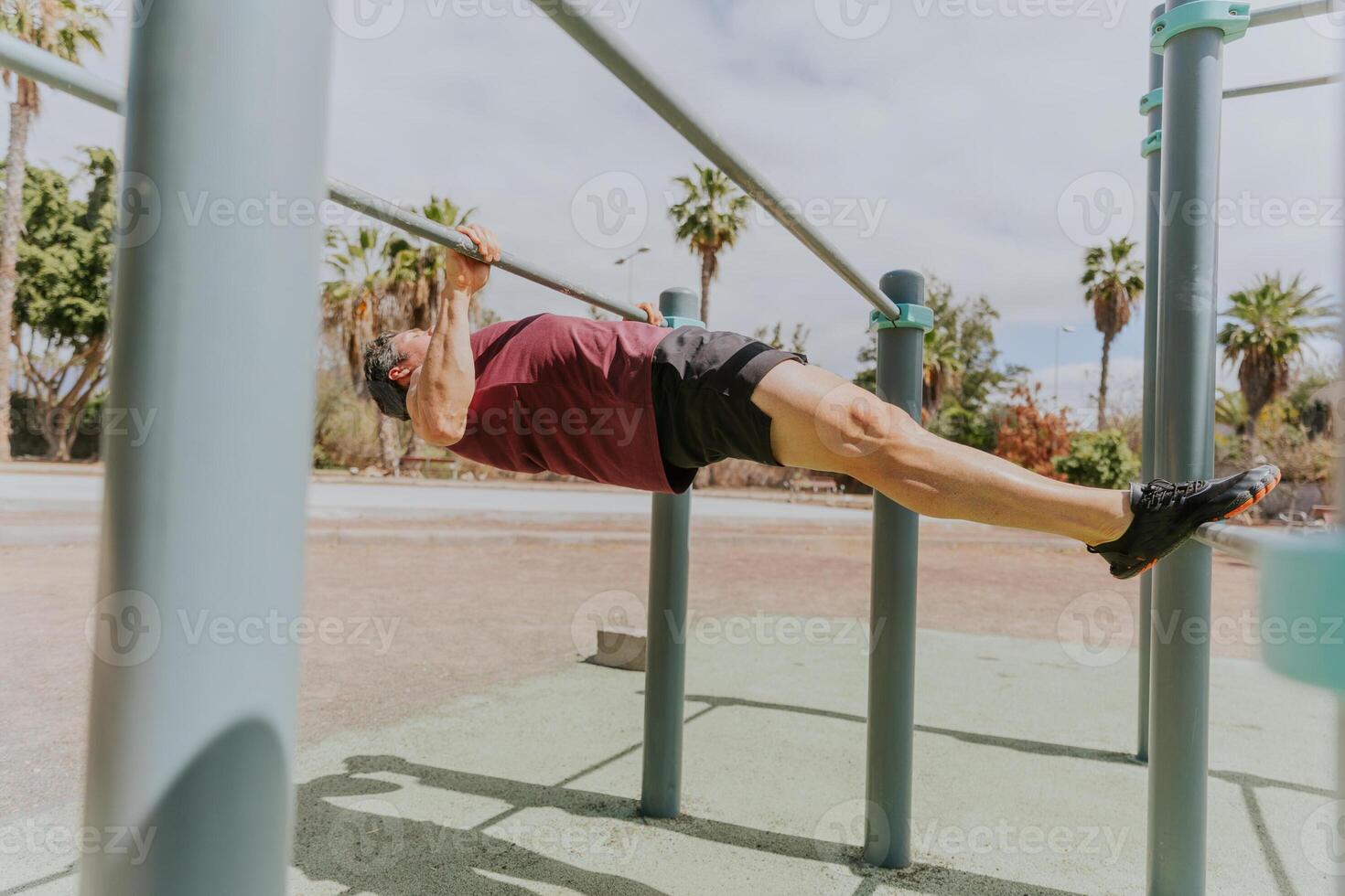 A strong man is doing Australian pull ups at a calisthenics outdoor gym in a tropical location photo