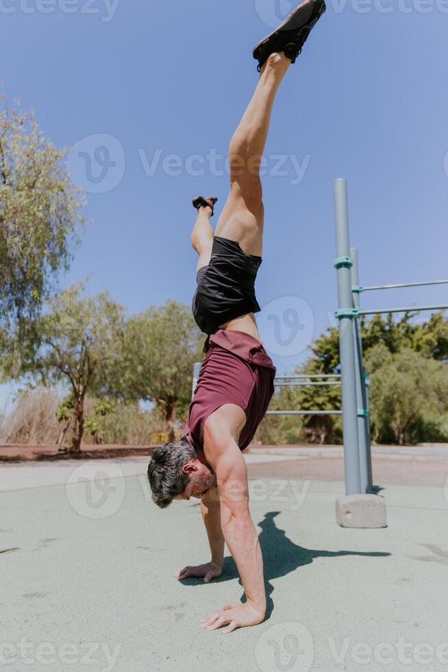A man is holding an handstand pose with open legs during a workout session outdoors photo