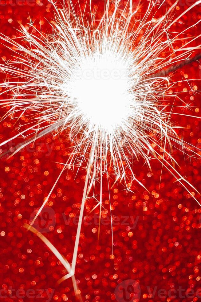 New Year celebration. Sparkler on red background. Christmas night. Bright sparks of fire and bokeh photo