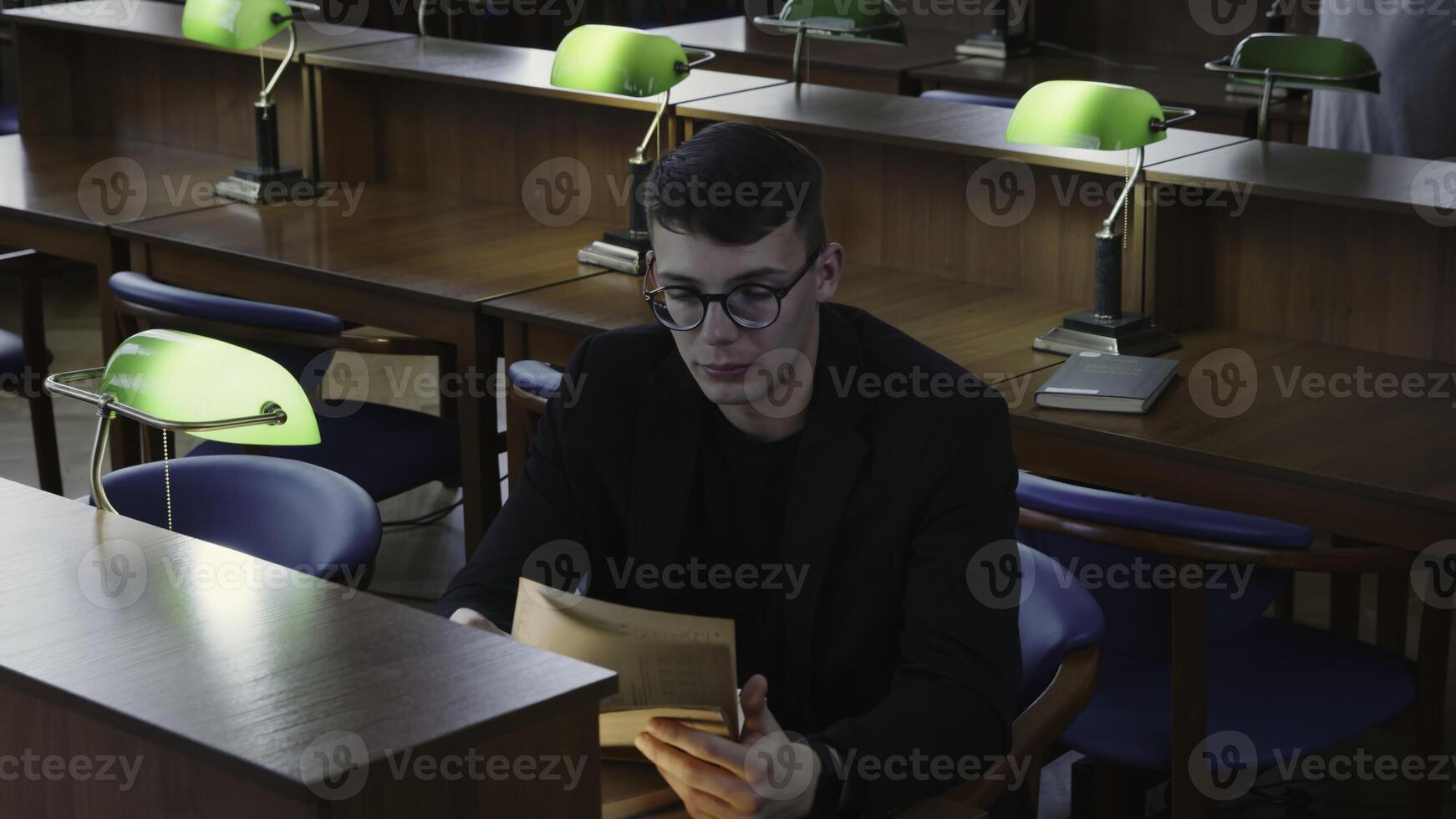 A dedicated student is engaged in focused study at a library desk, surrounded by books. Media photo