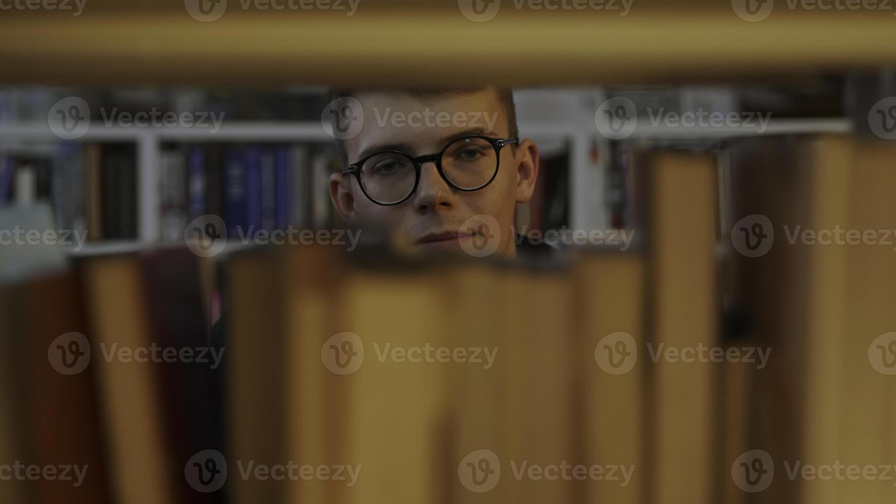 A thoughtful reader sits in a library, surrounded by books and shelves, engaging in reflection. Media photo