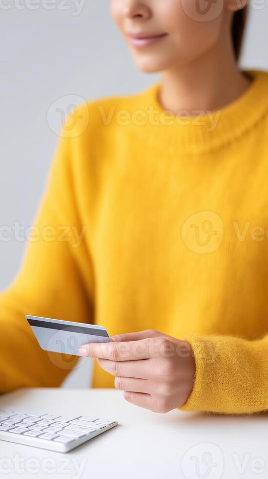 Woman holding credit card while using calculator in bright yellow sweater, financial planning and budgeting concept photo