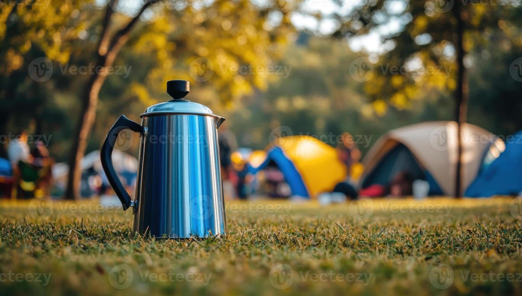 Metallic coffee pot resting on grassy campground, sunset illuminating camping scene behind photo
