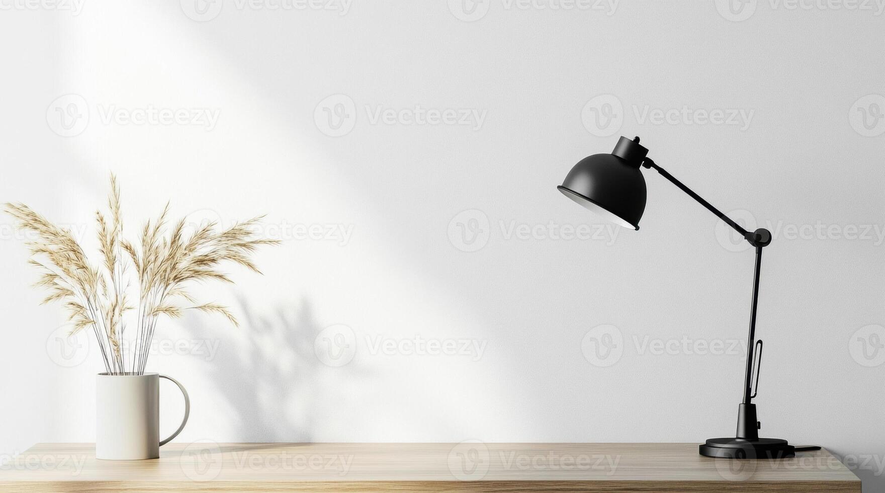 Sleek workspace featuring black lamp, pampas grass vase, natural light revealing shadows on pristine white wall photo