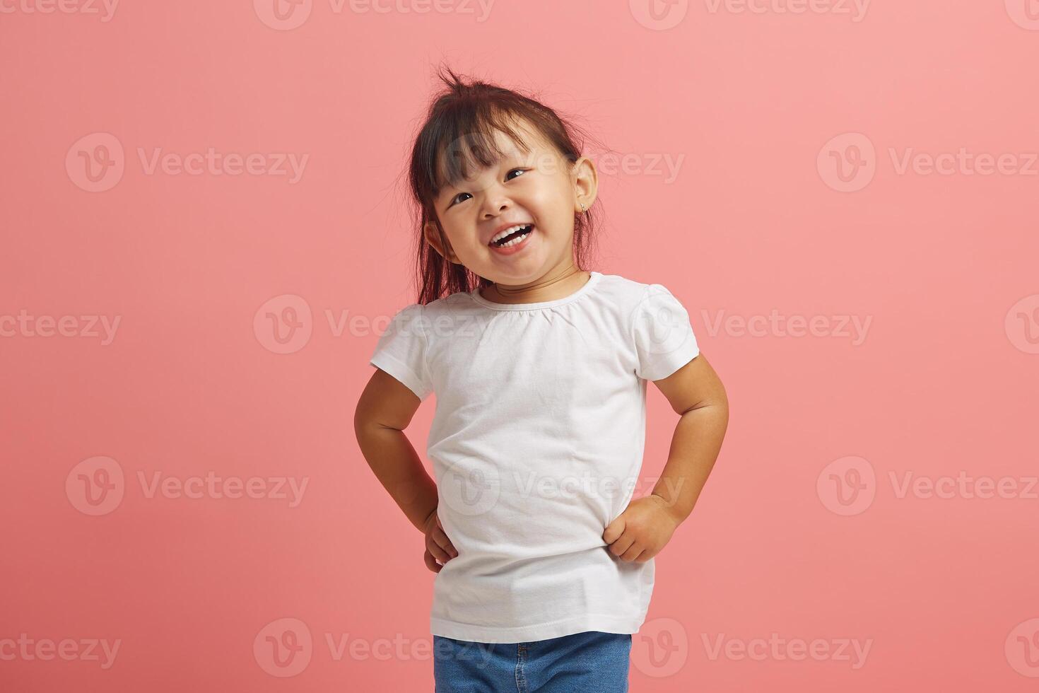 Cheerful three year old Asian girl smiles standing on pink isolated background. Beautiful Korean female child expresses a joyful mood on an isolated. photo