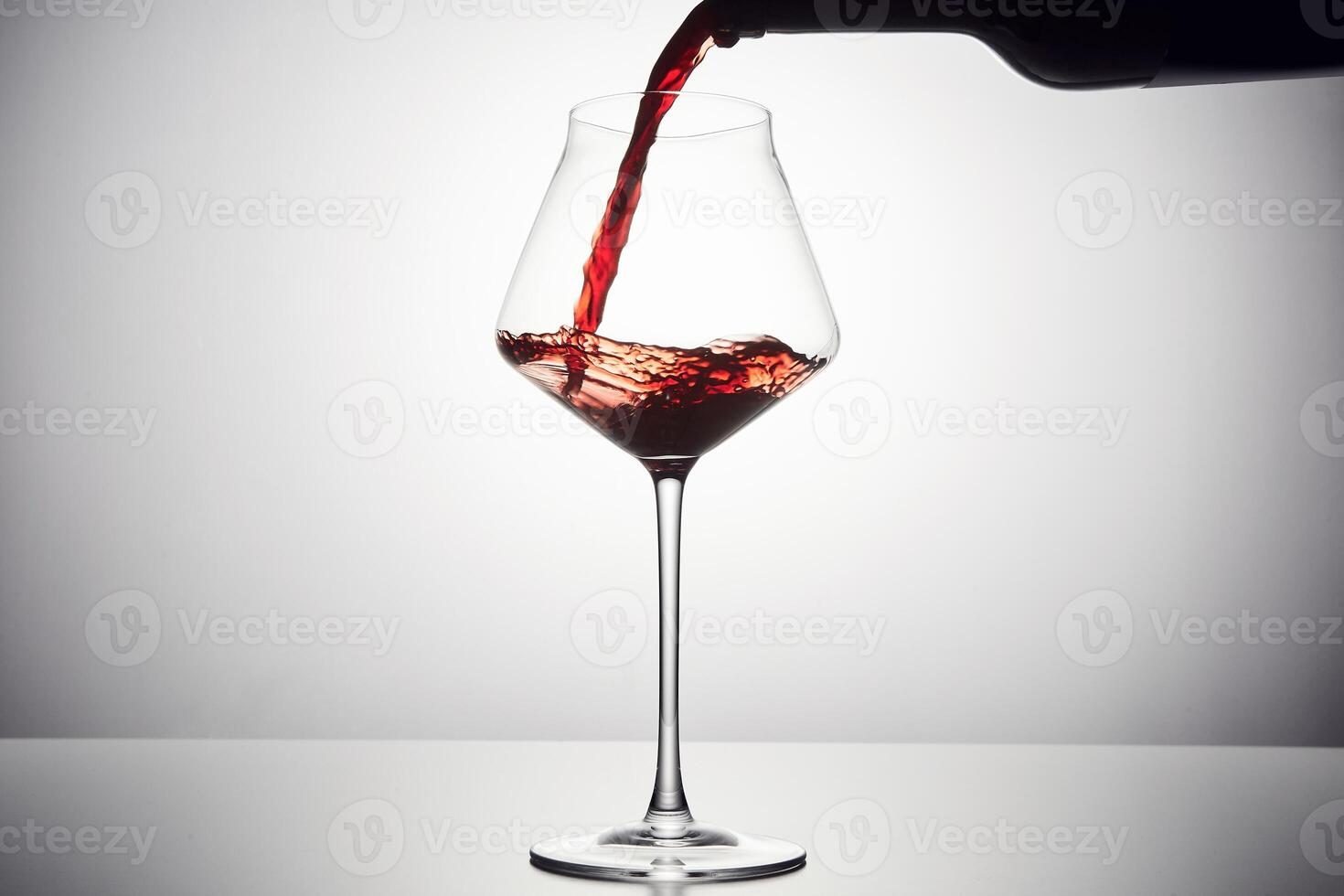 Red wine is poured from bottle into transparent glass. photo
