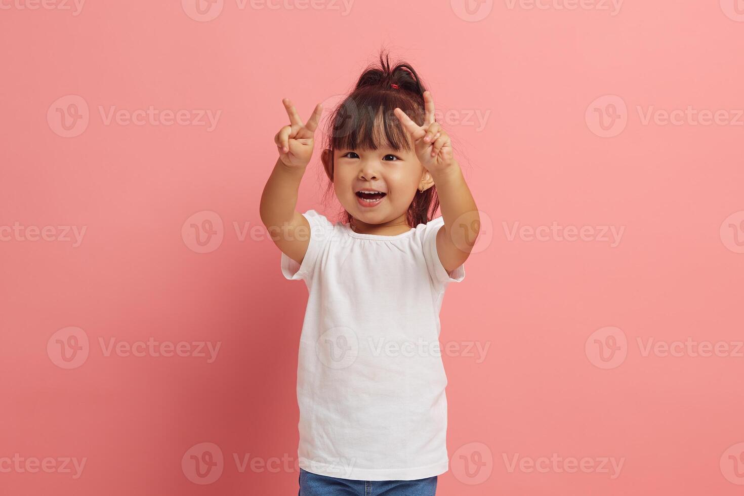 little asian etnicity funny girl showing V gesture with two hands standing over pink isolated background. photo