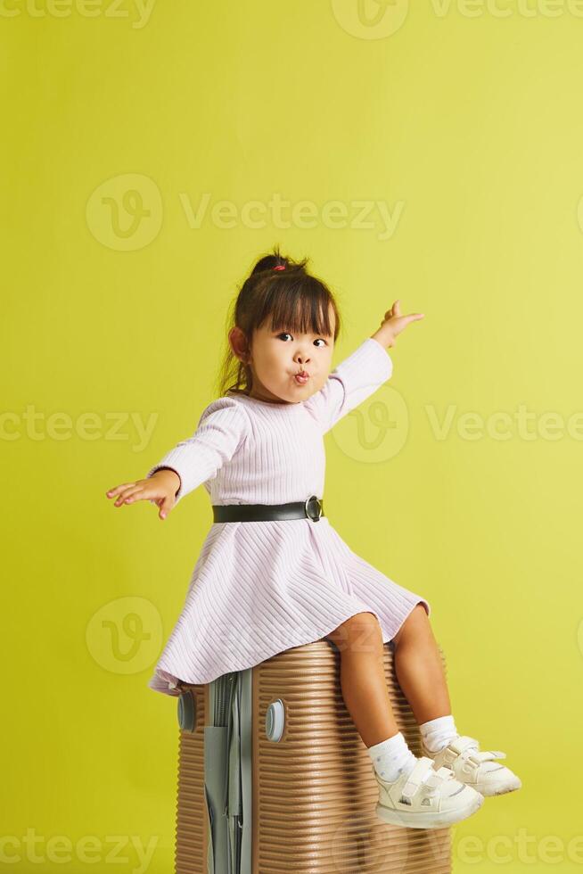Cheerful little asian ethnicity girl sitting on suitcase open herself arms to the sides like an airplane, looking forward to vacation and trip to the sea, loves to relax. photo