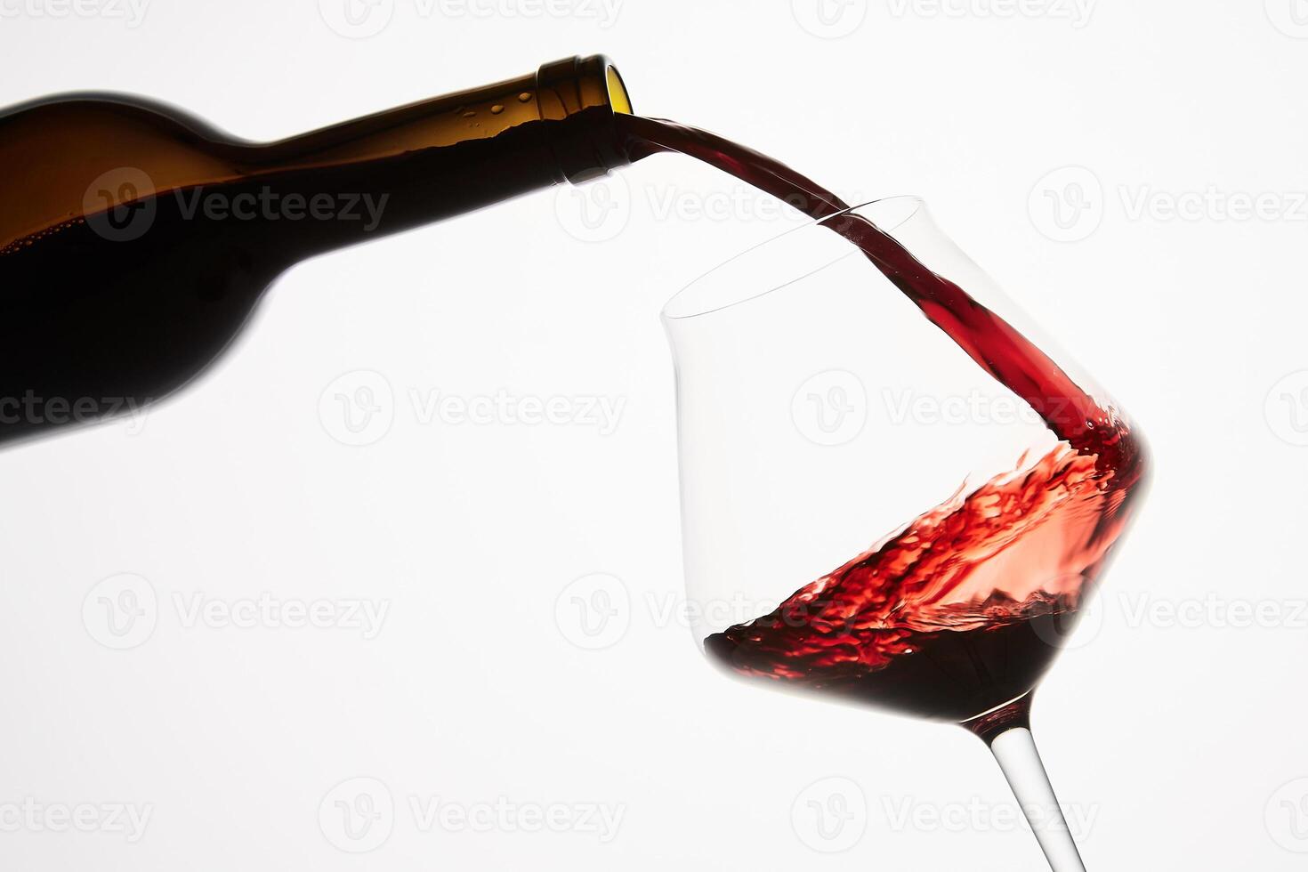 Red wine pouring into tilted wineglass from bottle. photo