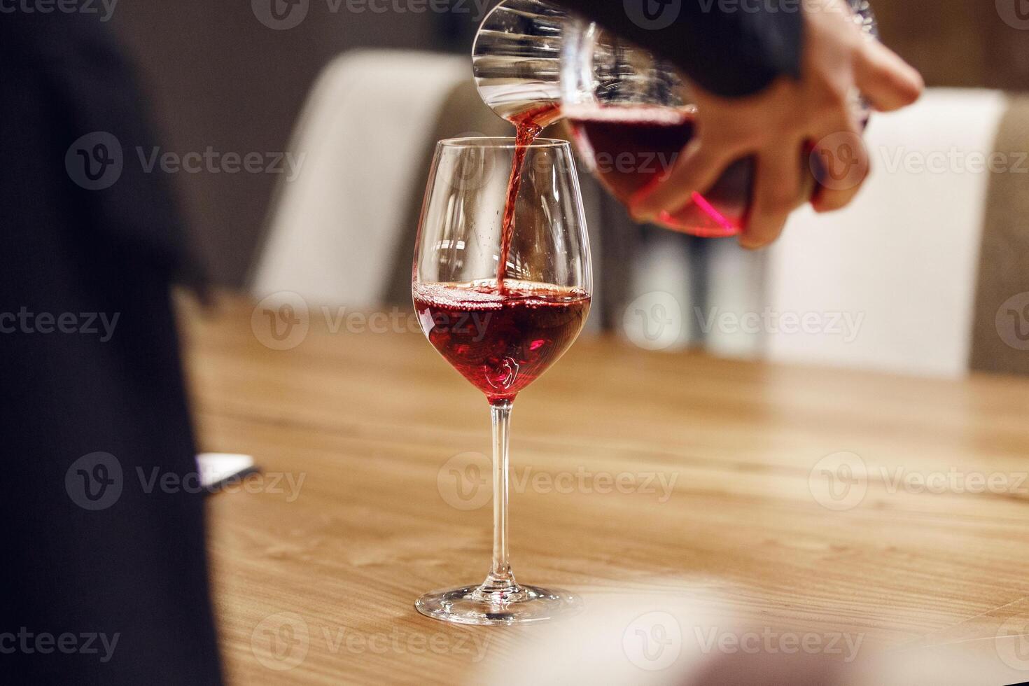 Bartender pouring red wine from decanter to the glass, close up image. photo