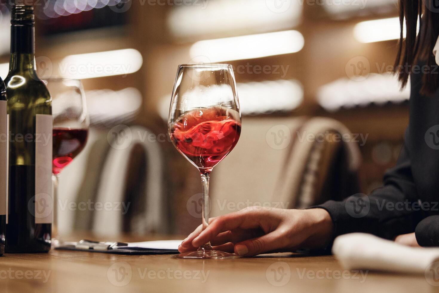 Female sommelier swirling red wine in glass on cellar background being in cellar. Wine expert exam to study different wine. photo