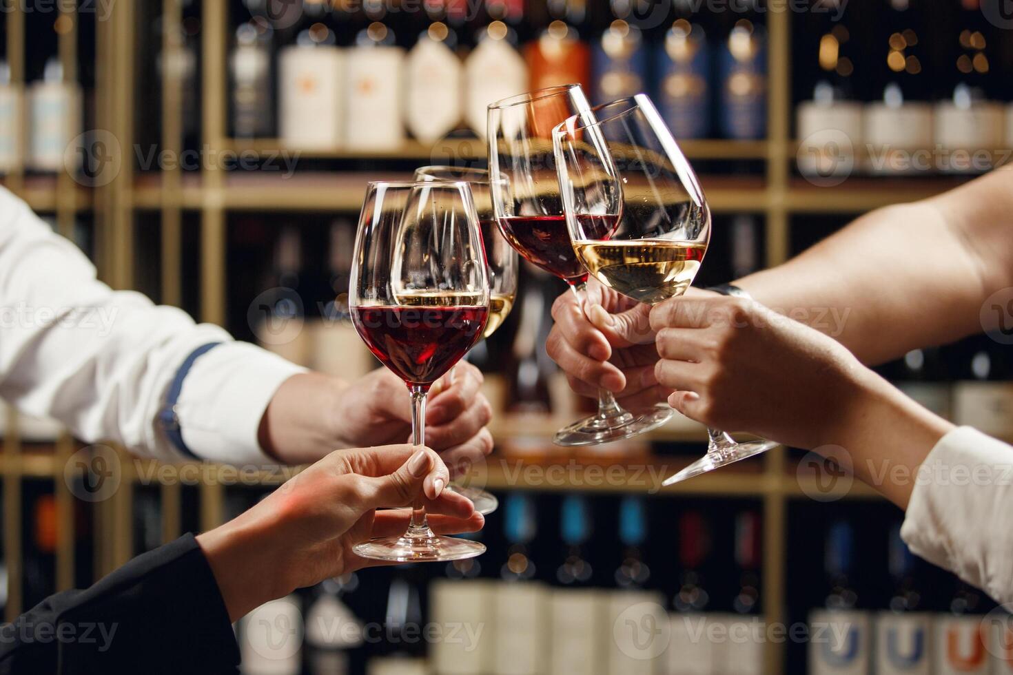 Big company people clinking glasses with red, rose and white wine on blurred cellar background. Men and women cheers with alcohol drink, closeup photo