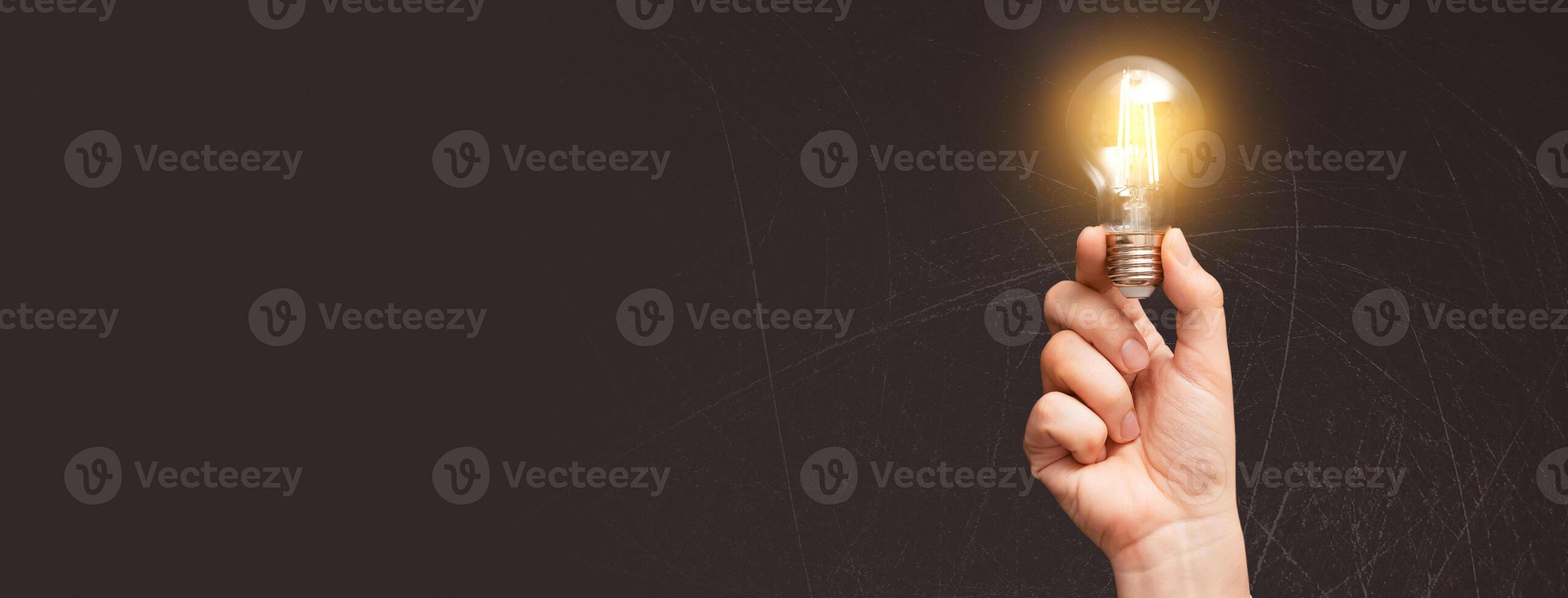 A hand holding a light bulb over a dark background photo