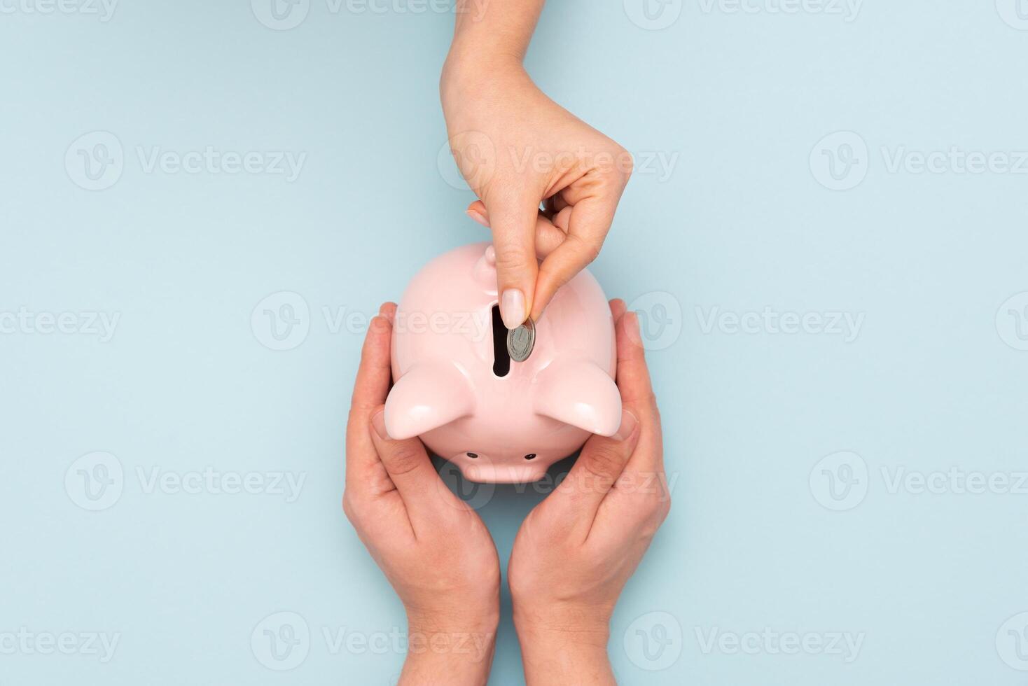 Two hands putting money into a piggy bank on a blue background photo