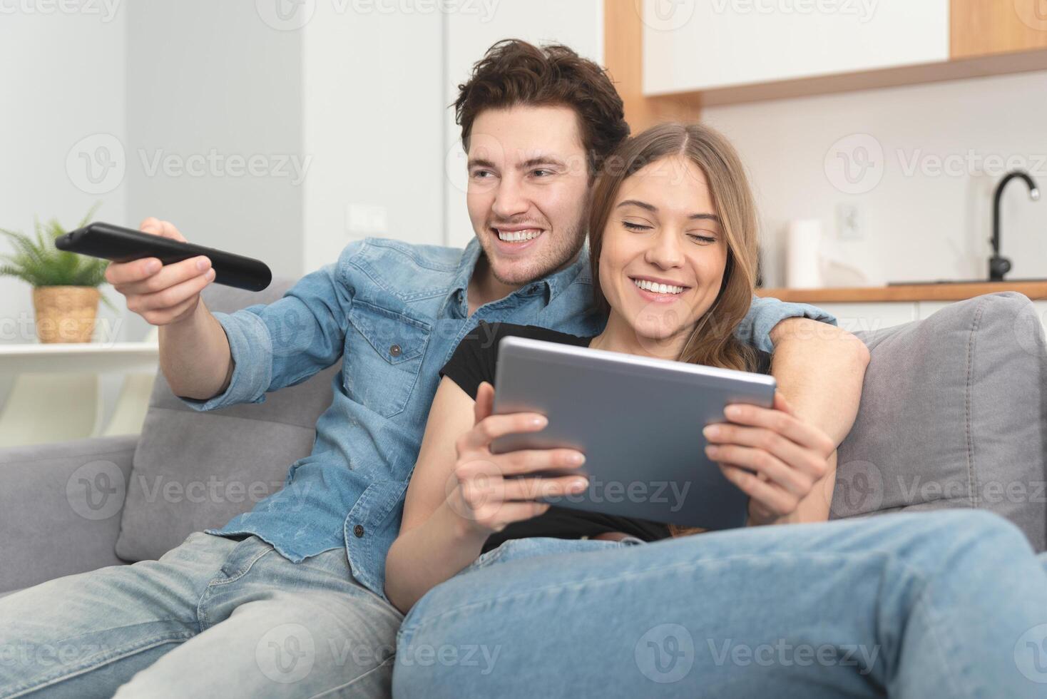 A man and woman sitting on a couch with a tablet and remote control photo