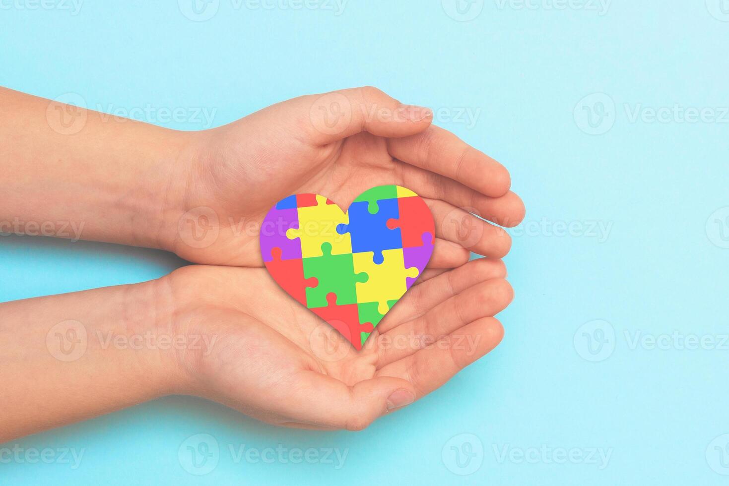 Two hands holding a colorful puzzle piece heart on a blue background photo
