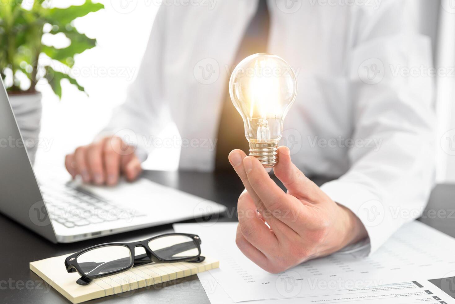 A man is holding a light bulb in front of a laptop photo