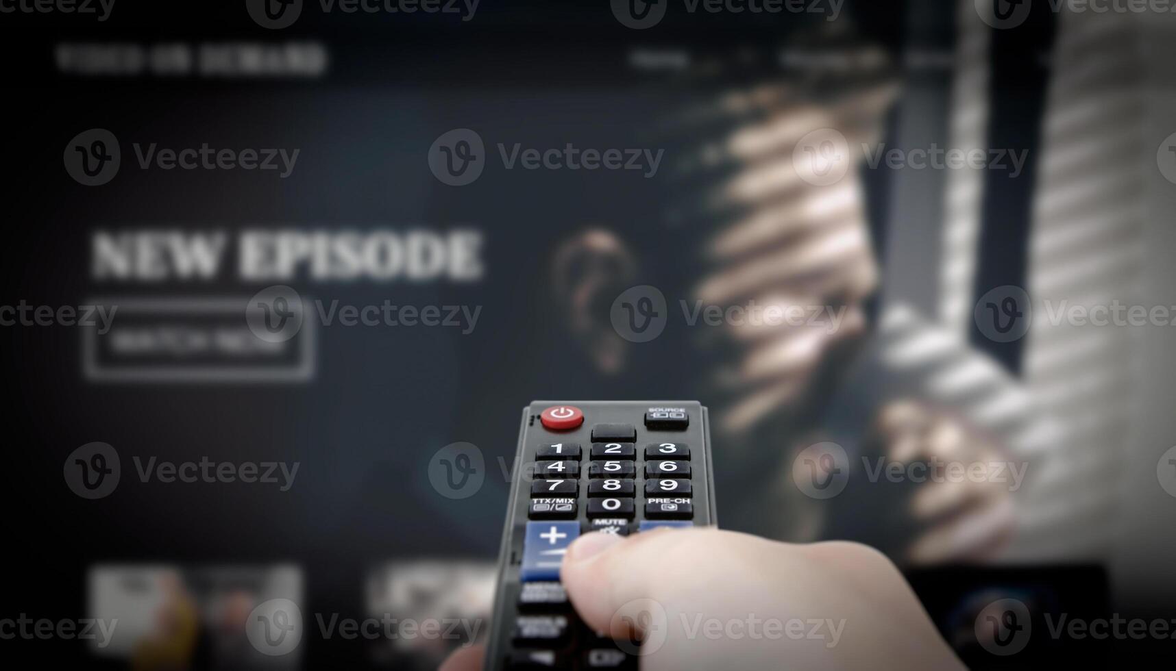 A hand holding a remote control, VOD screen in background photo