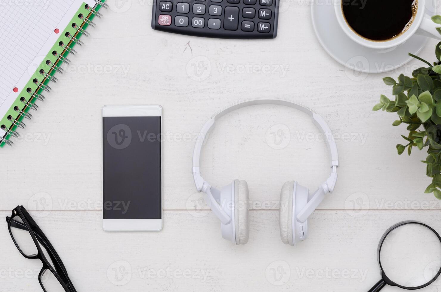 Top view of headphones, phone, calculator, and coffee on a white table photo