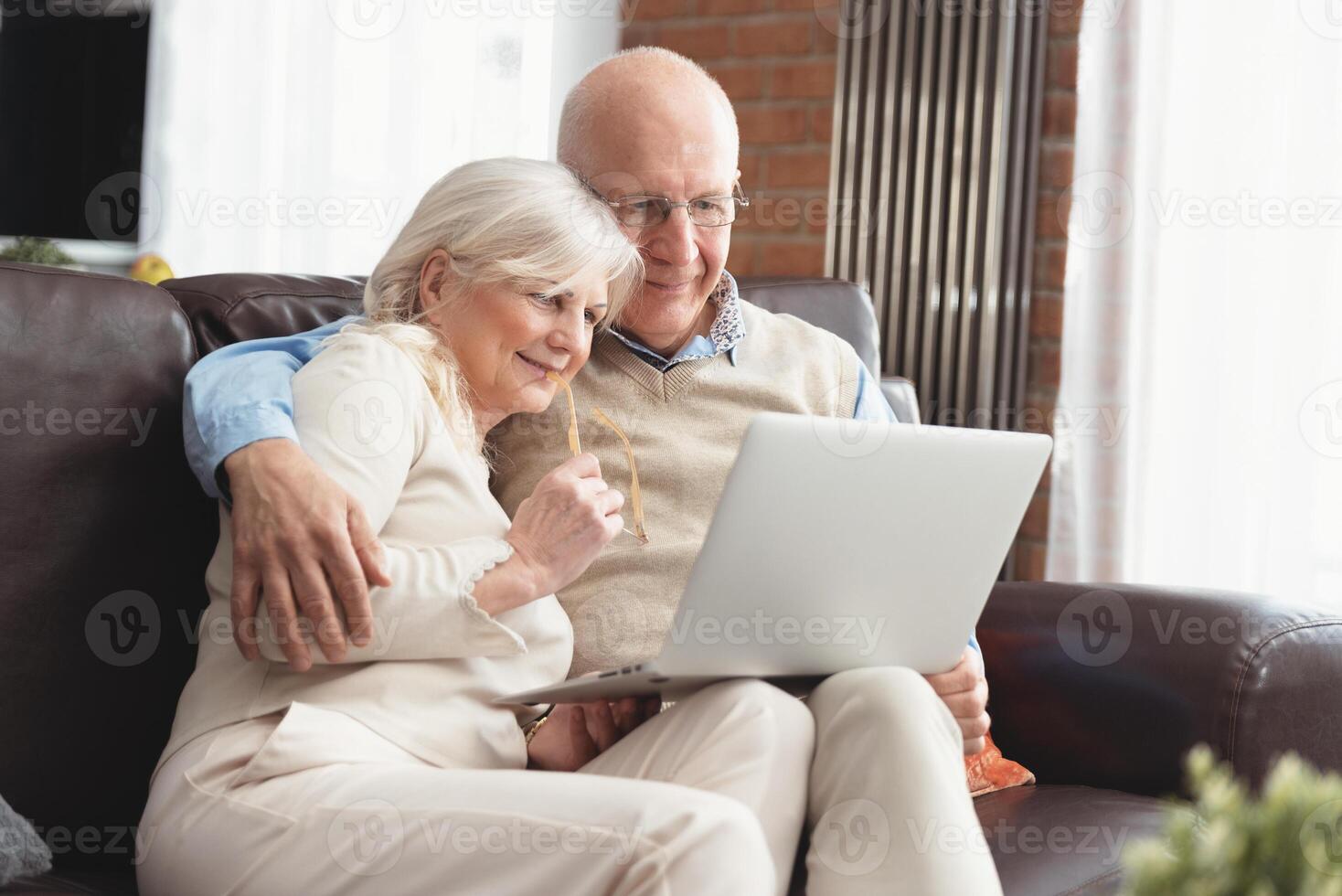 An older couple sitting on a couch with a laptop photo
