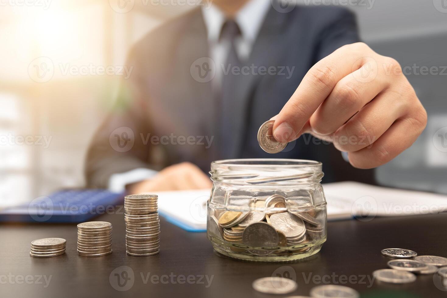 Man putting coins in jar on desk photo